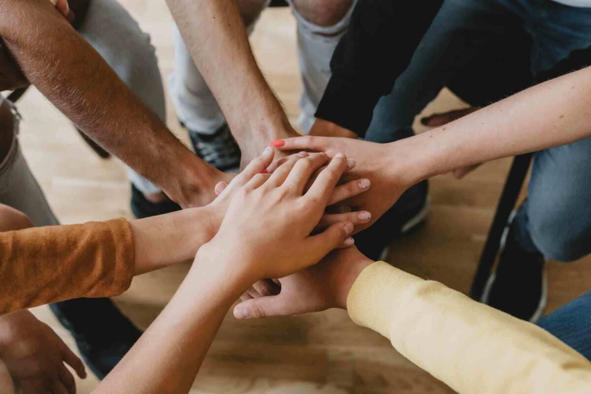 photo of participants in therapy putting their hands together as they discuss the benefits of teen group therapy